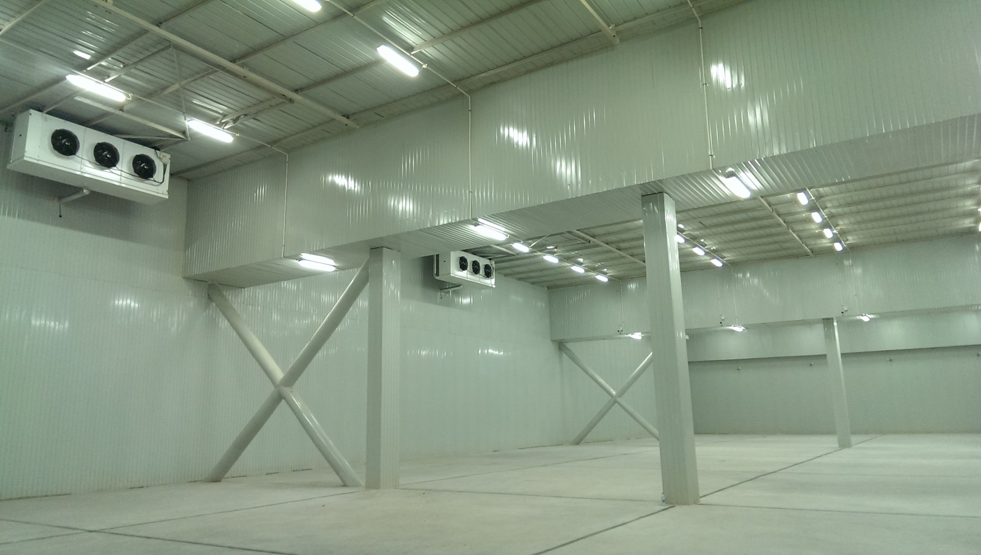 An open room interior with insulated wall and ceiling panels. Ceiling-mounted air coolers and exposed support beams are visible above the floor.